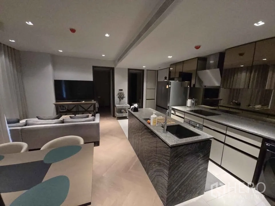 Condominium for rent in Watthana, Bangkok - Open-plan living room with L-shaped sofa, dining set and stone island kitchen.