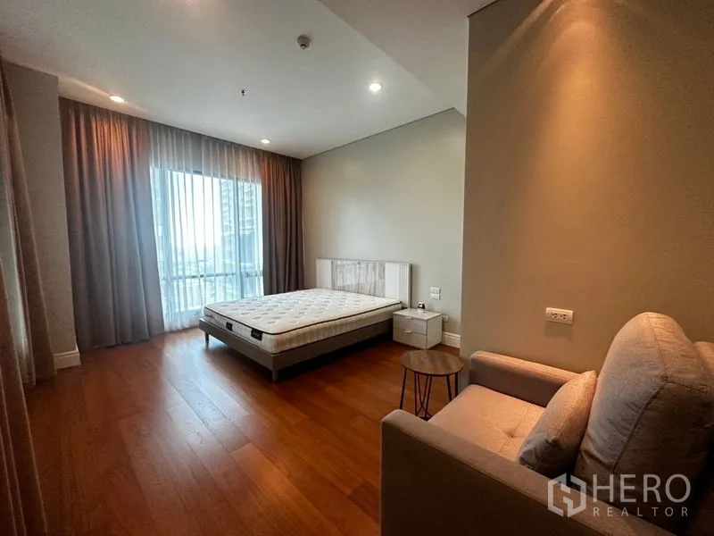 คอนโด ให้เช่าในKhlong Toei, Bangkok - ห้องนอนกว้างพร้อมหน้าต่างบานใหญ่ เตียง โซฟา และพื้นไม้สีน้ำตาลอบอุ่น