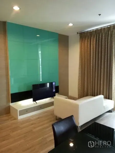 Condominium for rent in Ratchathewi, Bangkok - Bright living room with white sofa, TV console, teal glass feature wall, wood floors and full-length curtains.