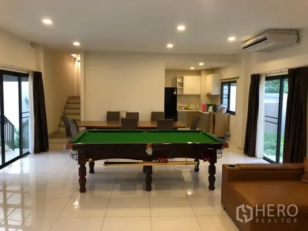 Townhouse for rent or sale in Saphan Sung, Bangkok - Open-plan living and dining area with a pool table, recessed lights and sliding glass doors.