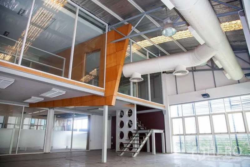货栈 出租在Prawet, Bangkok - 玻璃幕墙夹层办公室，金属楼梯、大窗与白色风管，位于工业仓库内。
