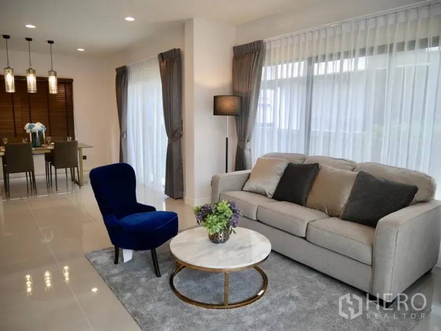 Detached House for rent in Bang Kapi, Bangkok - Bright open-plan living and dining area with sofa, blue accent chair, sheer curtains and pendant lights.