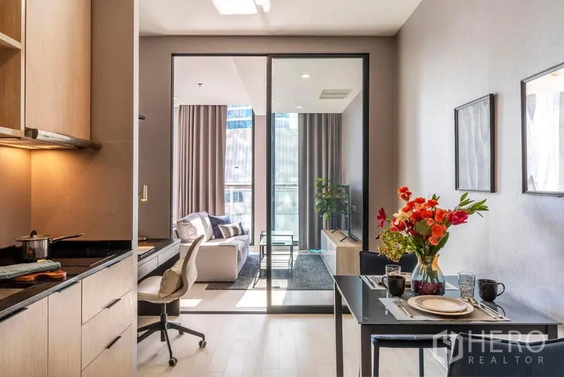 คอนโด ให้เช่าในPathum Wan, Bangkok - วิวจากครัวสู่ห้องนั่งเล่นผ่านประตูกระจกเลื่อน พร้อมโต๊ะกินข้าวสองที่และแจกันดอกไม้