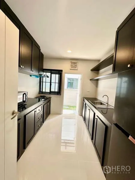 บ้าน ให้เช่าในBang Phli, Samut Prakan - ครัวรูปตัวแกลเลอรี ตู้สีดำ เตาแก๊ส อ่างล้างจาน หน้าต่าง และทางออกหลังบ้าน