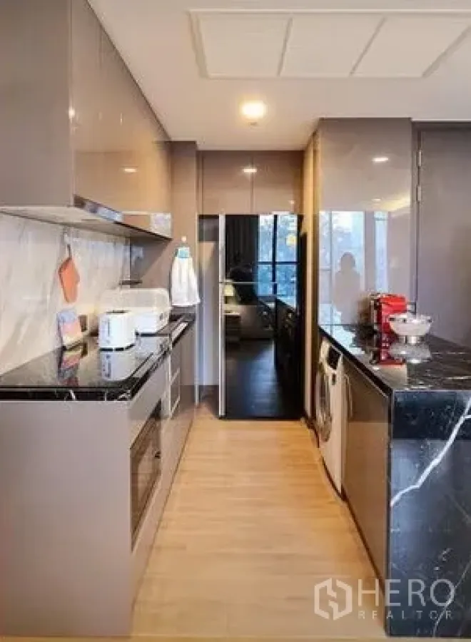 公寓 出租在Khlong Toei, Bangkok - 廊式厨房，亮面橱柜与黑色石材台面，内置烤箱、冰箱和洗衣机