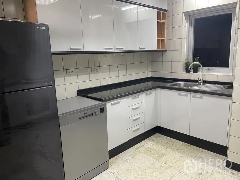 Condominium for rent or sale in Pathum Wan, Bangkok - U‑shaped kitchen with glossy white cabinets, black countertops, fridge, dishwasher and window over the sink.