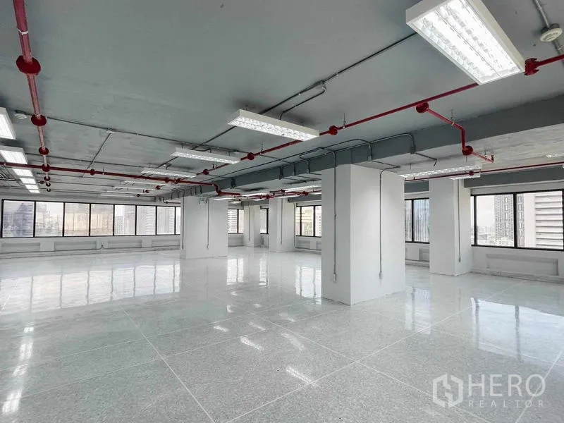 Office Space for rent in Bang Rak, Bangkok - Bright open-plan office floor with polished tiles, exposed ceiling and red sprinkler pipes, surrounded by windows with Bangkok skyline views.