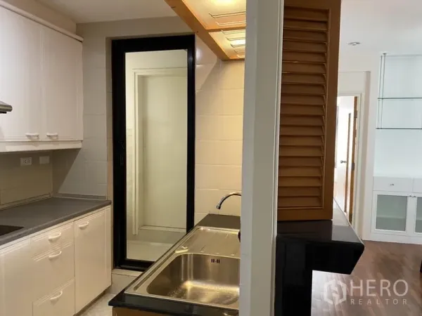 公寓 出租或出售在Sathon, Bangkok - 长廊式厨房，不锈钢水槽、白色橱柜，滑动玻璃门通向工作阳台