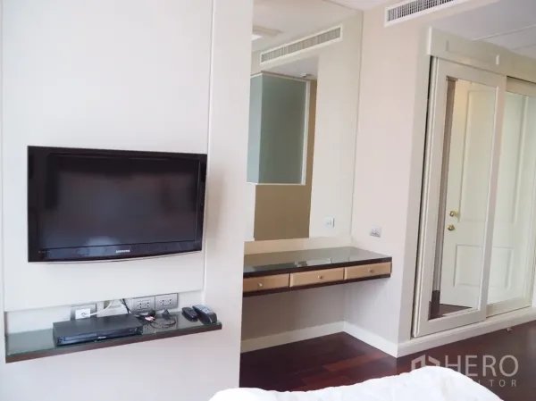 Condominium for rent in Pathum Wan, Bangkok - Bedroom corner featuring a wall‑mounted TV, glass shelf, built‑in vanity and mirrored wardrobe doors.