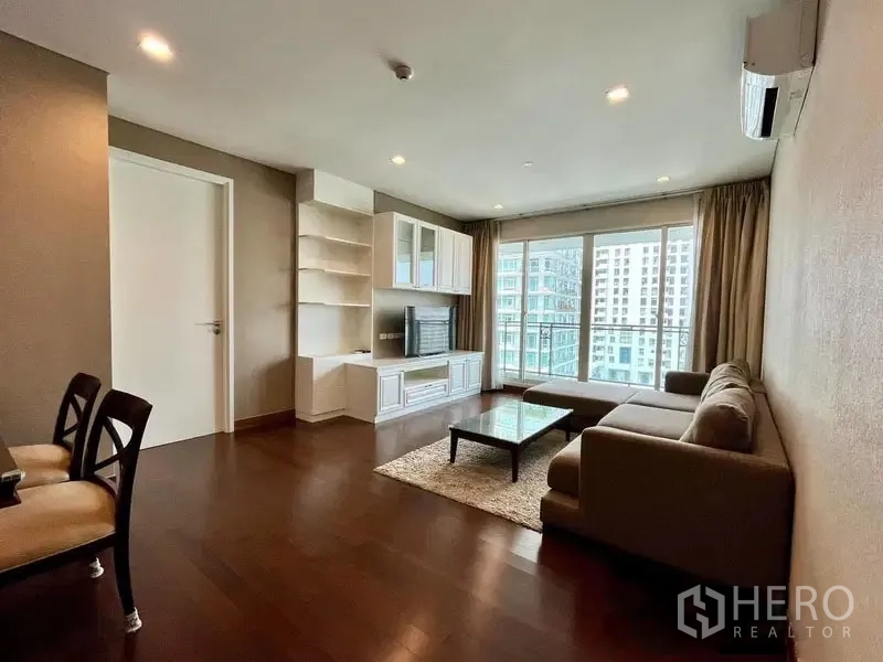 Condominium for rent in Watthana, Bangkok - Spacious lounge with wooden floors, balcony doors, TV wall, and city view.