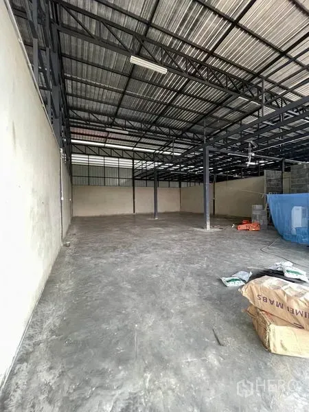货栈 出租在Pathum Thani - 纵深视角的空置仓储空间，金属屋顶，地面有工具材料。