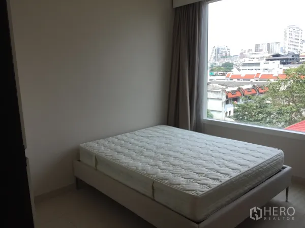 Condominium for rent or sale in Watthana, Bangkok - Sunlit bedroom with a large picture window overlooking the Sukhumvit cityscape in a Watthana condo.