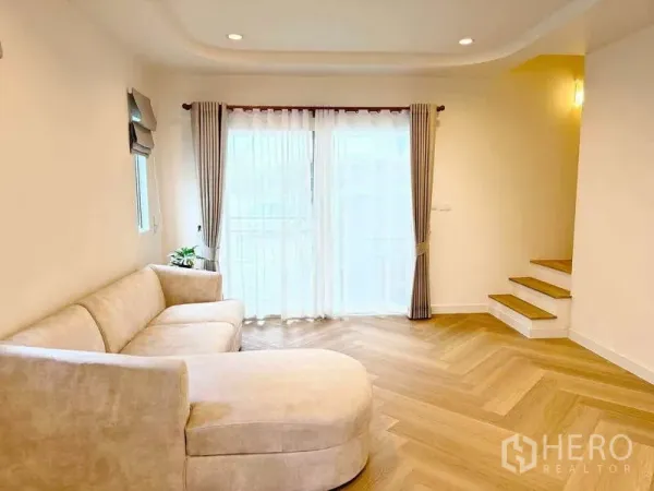 ทาวน์เฮาส์ ให้เช่าในSuan Luang, Bangkok - ห้องนั่งเล่นสว่าง พร้อมโซฟาเข้ามุมสีเบจ พื้นลายก้างปลา ประตูกระจกบานเลื่อน และบันไดสั้น