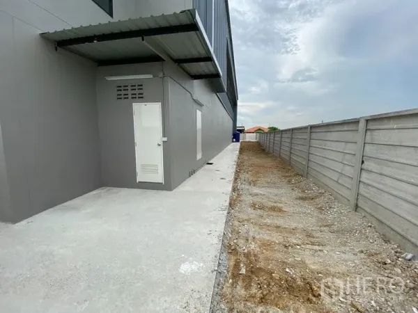 Warehouse for rent or sale in Bang Len, Nakhon Pathom - Side walkway with utility door along the warehouse and boundary wall.