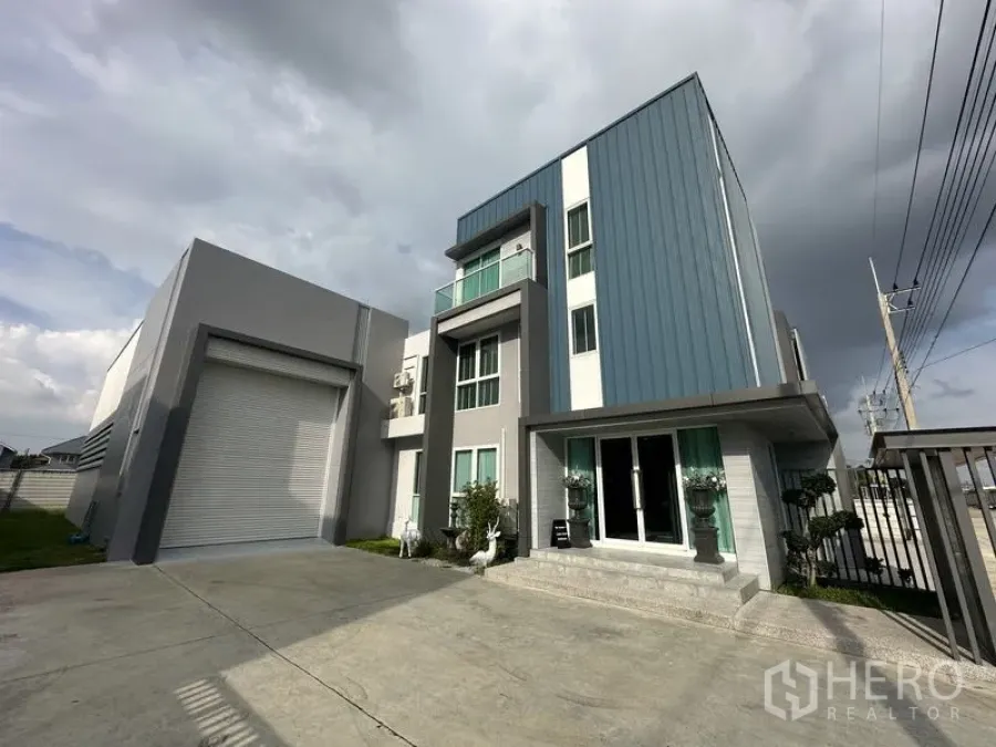 Factory for sale in Lam Luk Ka, Pathum Thani - Front driveway showing warehouse loading bay with roller shutter beside the three-storey office.