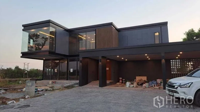 บ้าน ขายในChachoengsao - มุมใกล้ตัวบ้านสีดำทันสมัย ผนังกระจกบานใหญ่ โรงจอดรถกว้างพร้อมไฟดาวน์ไลต์ มีอุปกรณ์ก่อสร้างหน้าบ้าน