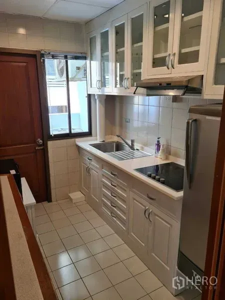 คอนโด ให้เช่าในWatthana, Bangkok - ครัวแบบแกลเลย์ตู้สีขาว ซิงค์คู่ เตาไฟฟ้า และหน้าต่าง ผนังปูกระเบื้อง