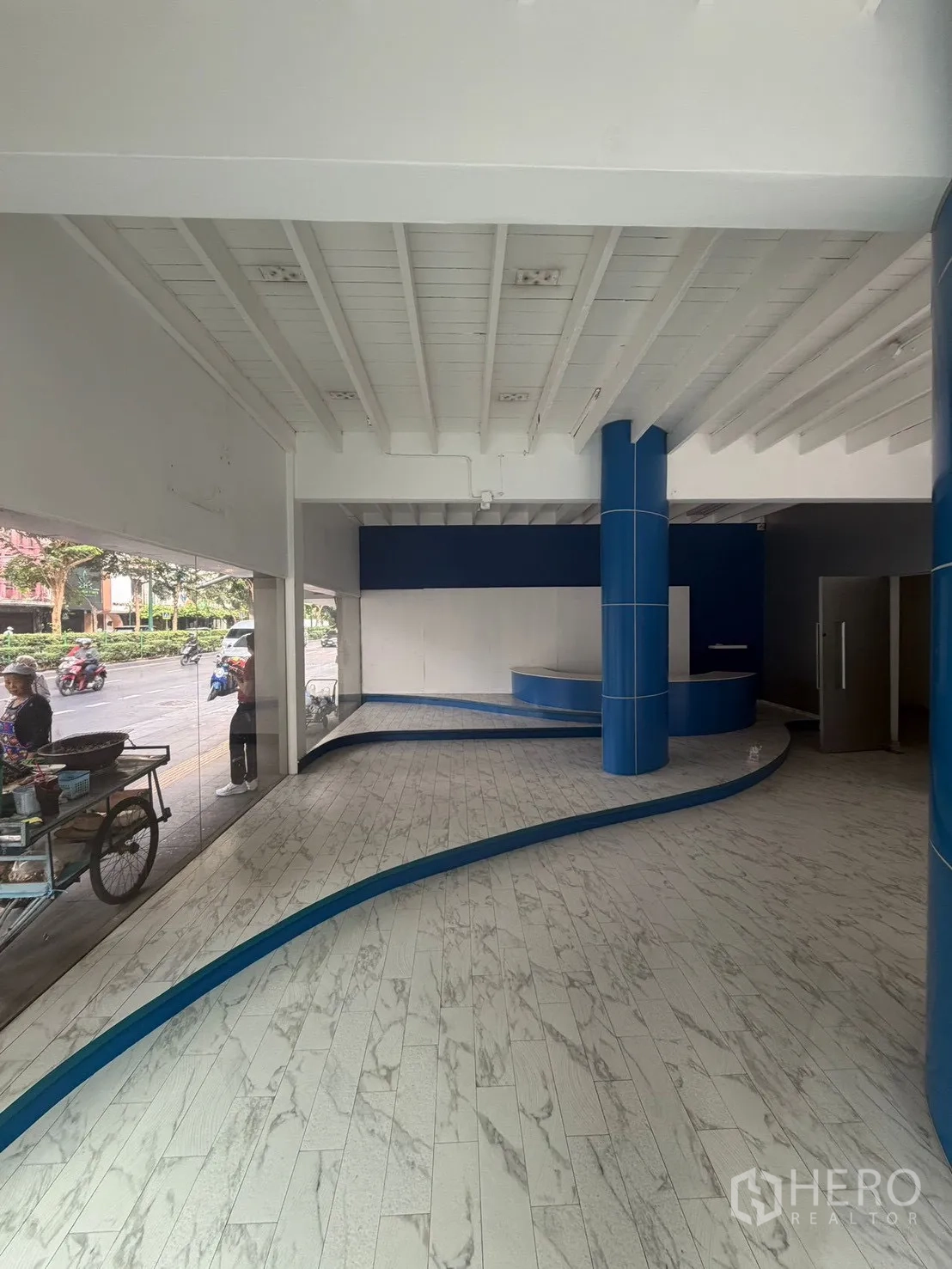 Shophouse for rent in Watthana, Bangkok - Ground-floor showroom with marble-look tiles, curved platform, and glass frontage.