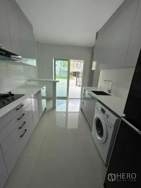 Townhouse for rent in Bang Phli, Samut Prakan - Galley kitchen with grey cabinetry, fridge, washer and sliding door.