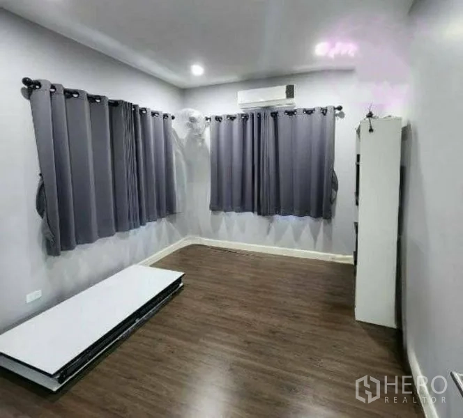 Detached House for sale in Pathum Thani - Flexible room with wood flooring, grey curtains and air conditioning.