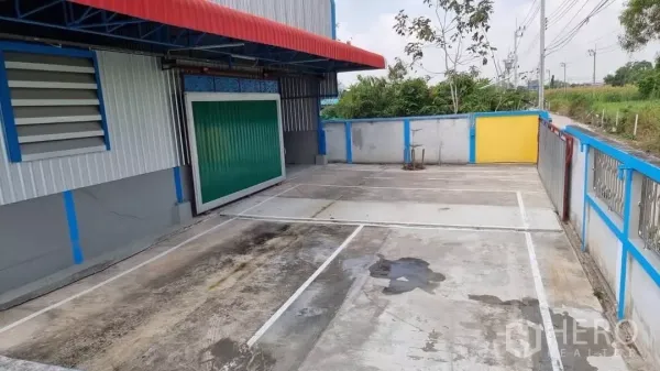 Warehouse for rent in Min Buri, Bangkok - Private concrete yard with marked parking bays, rolling green loading door and covered loading canopy.