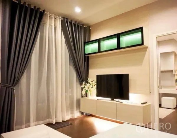 Condominium for rent in Ratchathewi, Bangkok - Living area with sheer curtains, wall-mounted cabinets and flat-screen TV.
