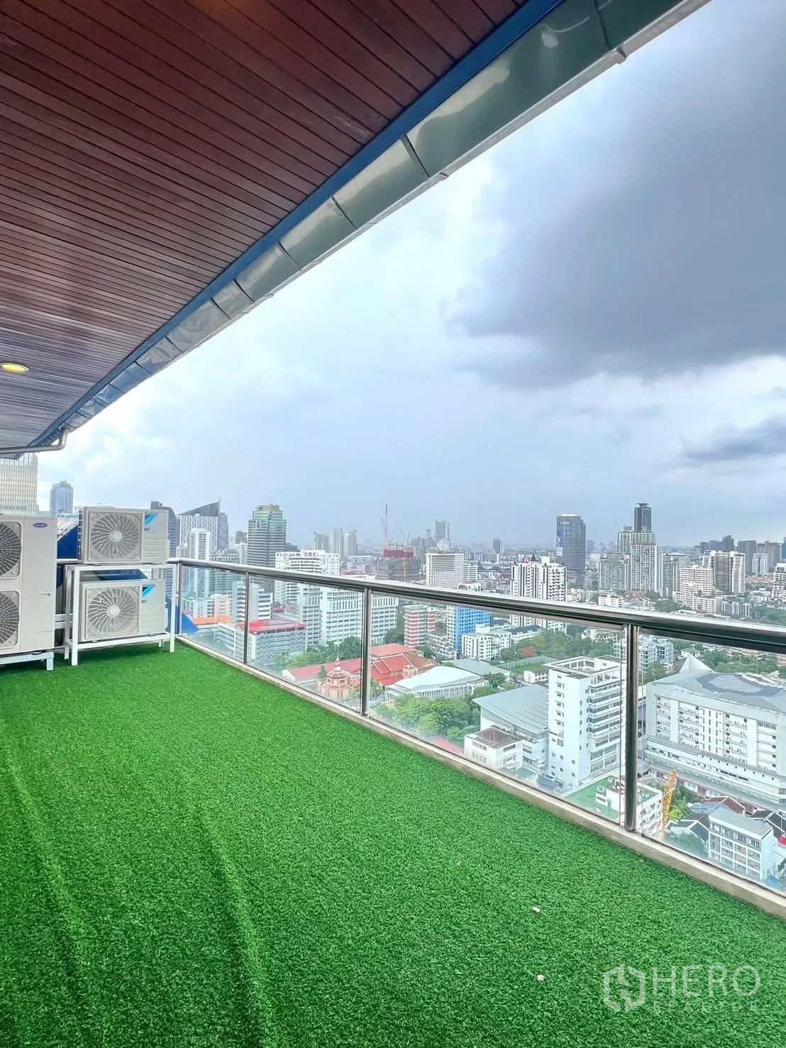 Condominium for rent in Khlong Toei, Bangkok - Long balcony with artificial grass and glass railing overlooking the city skyline.
