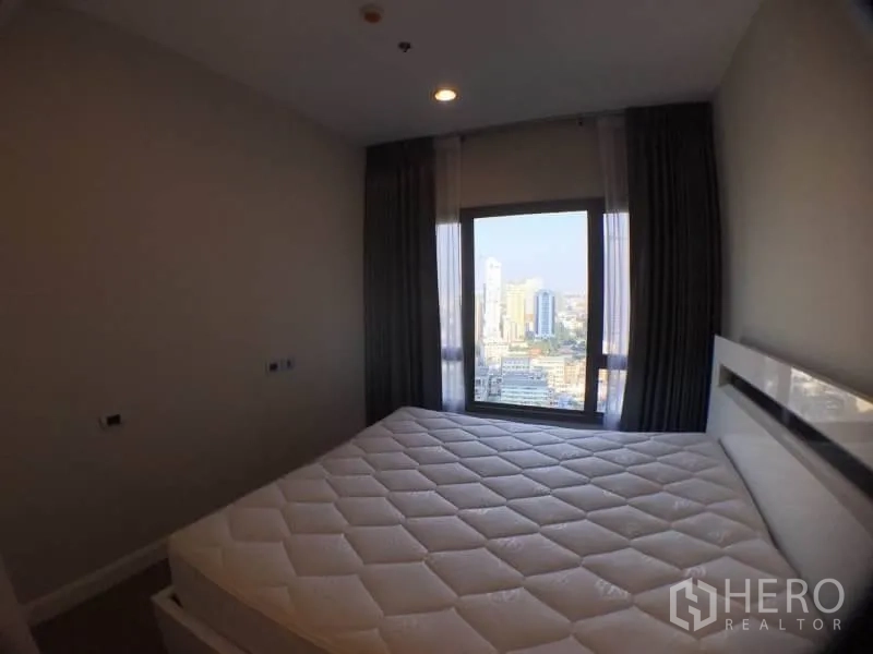 Condominium for rent in Khlong Toei, Bangkok - Bedroom with a large window framing Bangkok skyline views.