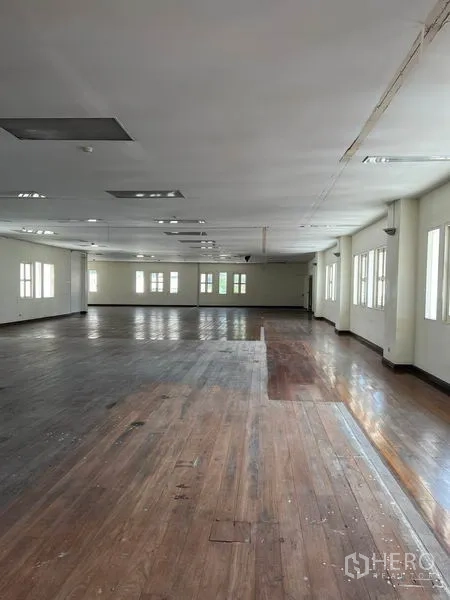 Office Space for rent in Khlong Toei, Bangkok - Long office hall with mixed-tone hardwood floors, multiple windows, and ceiling light panels across an open workspace.