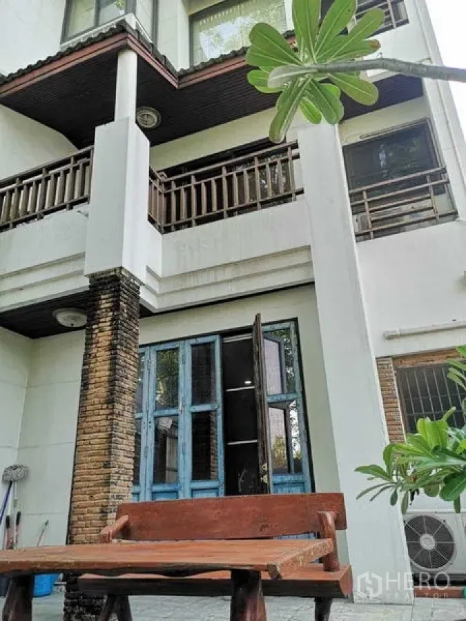 Townhouse for rent or sale in Suan Luang, Bangkok - Three-storey townhouse exterior with balconies, brick column and courtyard bench.
