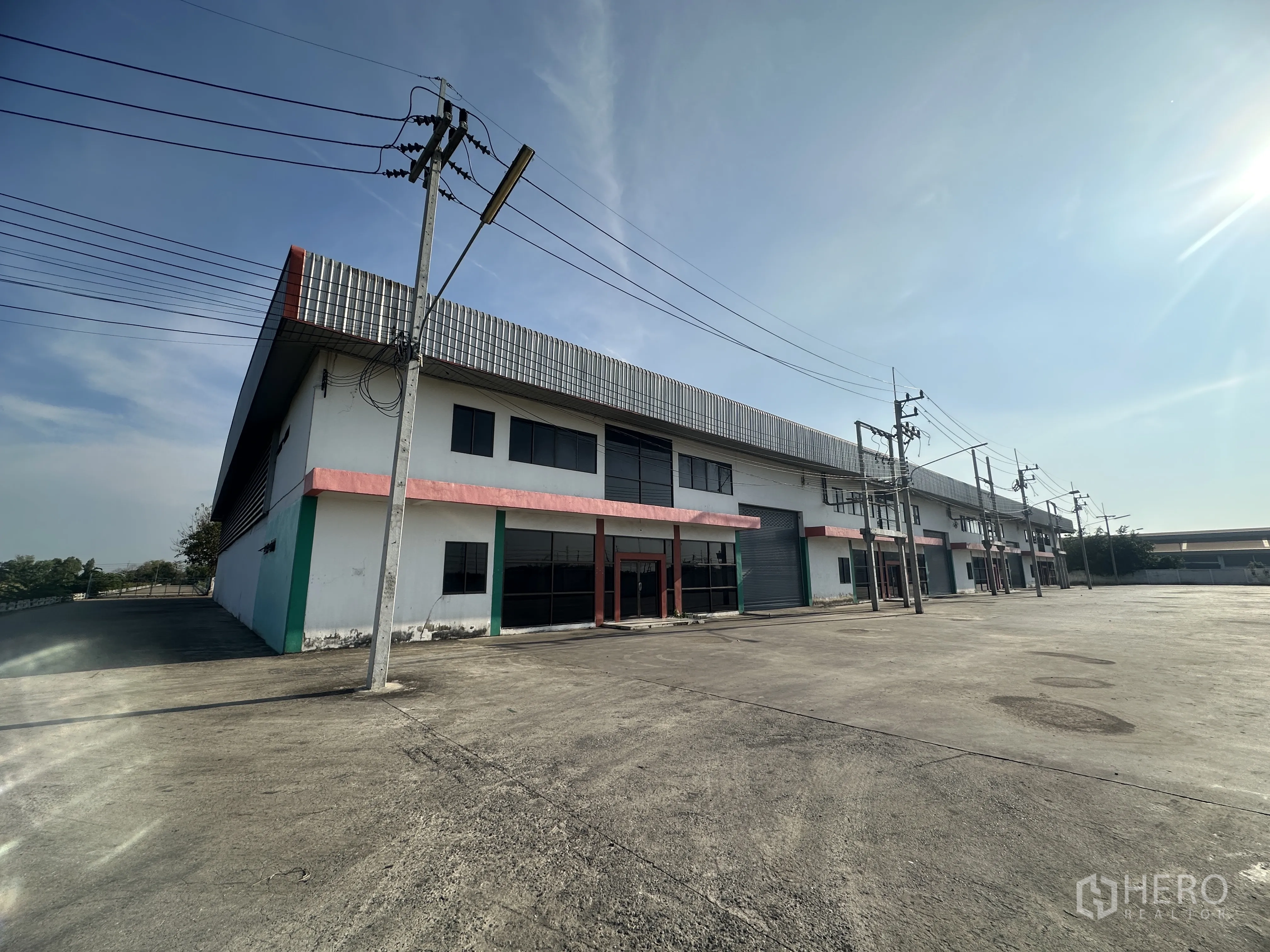 Factory for rent in Wang Noi, Phra Nakhon Si Ayutthaya - Corner view of factory row with glass-fronted offices, roller shutters, and a wide concrete yard.