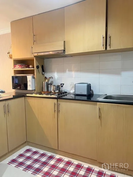 公寓 出售在Watthana, Bangkok - 配备木质橱柜、炉灶、抽油烟机与瓷砖挡板的曼谷公寓厨房。