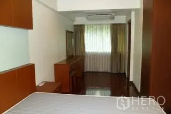 Condominium for rent in Pathum Wan, Bangkok - Bright bedroom with built-in wood cabinetry, desk, and a large curtained window over polished floors.