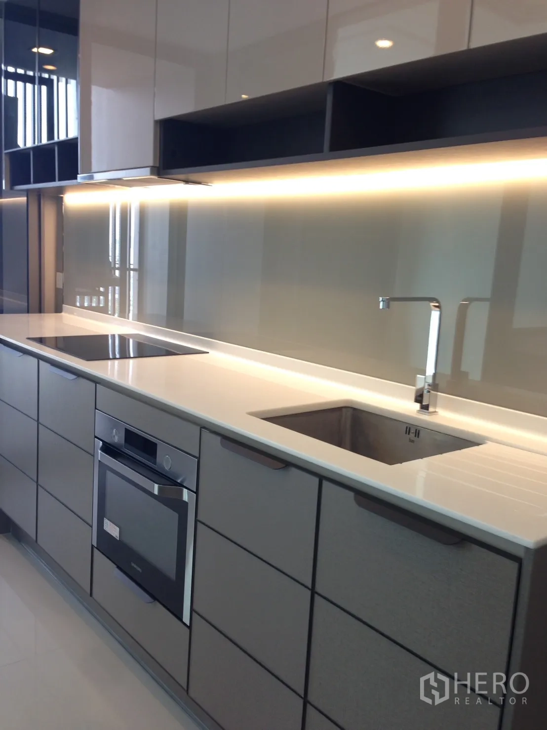 Condominium for rent in Bang Sue, Bangkok - Sleek linear kitchen with induction hob, built-in oven, sink and under-cabinet lighting.