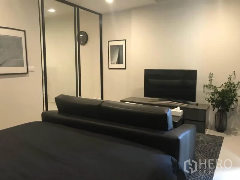 Condominium for rent or sale in Pathum Wan, Bangkok - Bedroom and living space with black sofa facing TV console and glass partition walls.