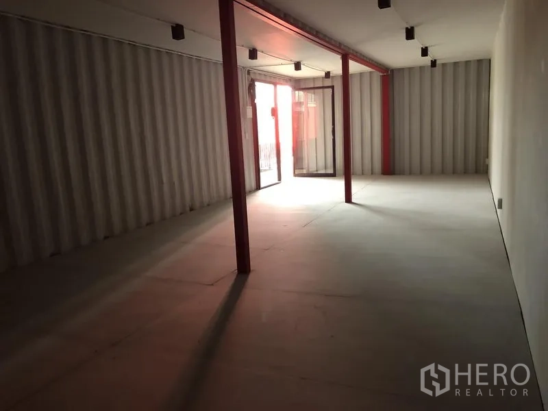 Office Space for rent in Khlong Toei, Bangkok - Long industrial office interior with red support columns, track lighting and sliding glass entrance.