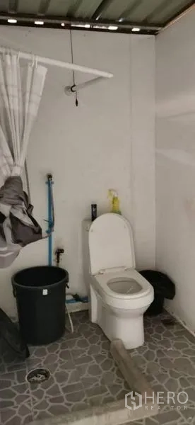 Warehouse for rent in Huai Khwang, Bangkok - Simple restroom with toilet, tiled floor, and exposed plumbing inside the warehouse.