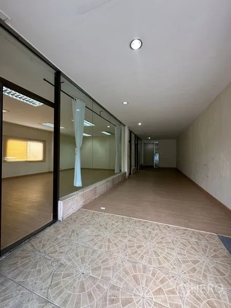 Warehouse for rent in Suan Luang, Bangkok - Ground-floor corridor with glass partitions and tiled entry, suitable for showroom access.