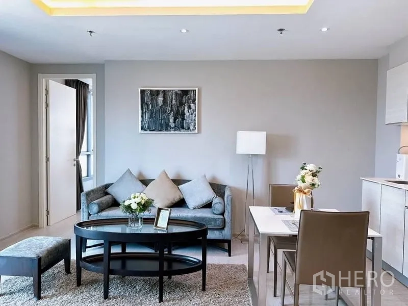 คอนโด ให้เช่าในWatthana, Bangkok - โซนนั่งเล่นมีโซฟา โต๊ะกลางรูปวงรี และชุดทานอาหารสำหรับสองคนข้างครัว