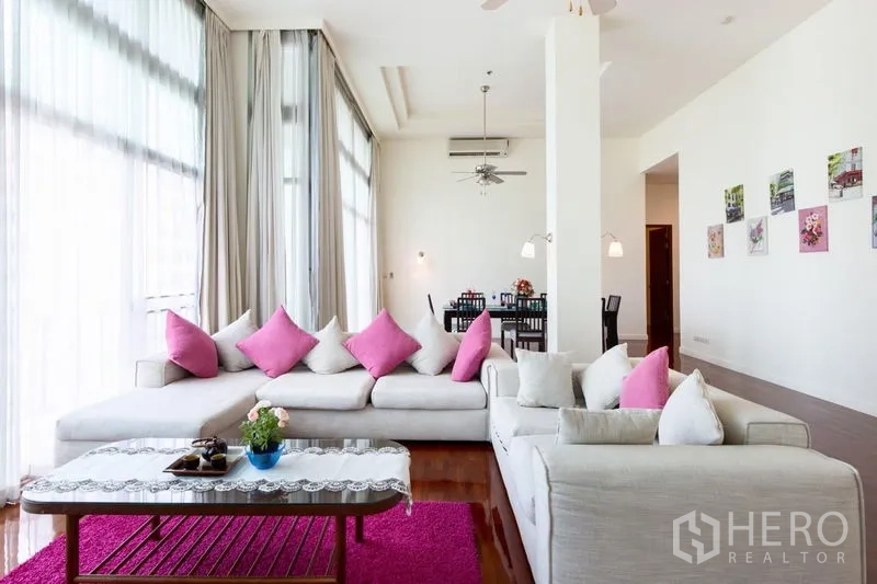 Condominium for rent in Bang Rak, Bangkok - Sunlit lounge with white sofas and pink cushions, full-height windows and view toward the dining zone.