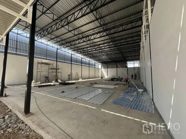 คลังสินค้า ให้เช่าในLam Luk Ka, Pathum Thani - ภาพภายในมุมข้าง พื้นที่โล่งกว้าง โครงหลังคาเหล็ก และวัสดุงานก่อสร้างบนพื้น