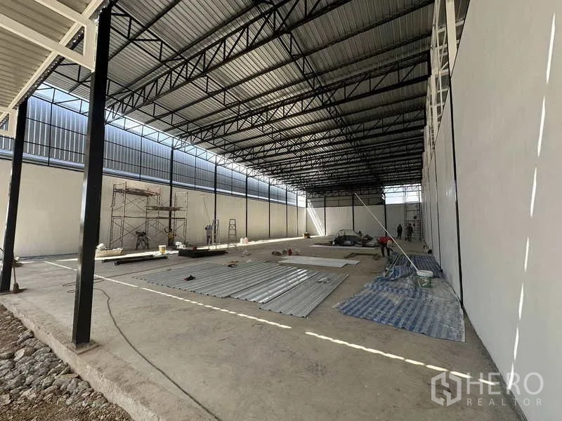 คลังสินค้า ให้เช่าในLam Luk Ka, Pathum Thani - ภาพภายในมุมข้าง พื้นที่โล่งกว้าง โครงหลังคาเหล็ก และวัสดุงานก่อสร้างบนพื้น