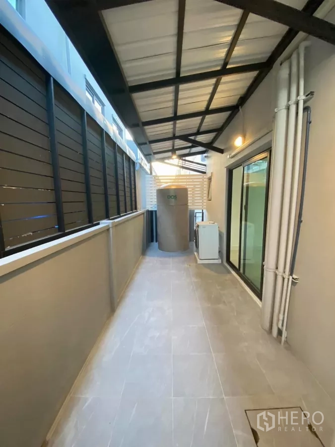 Townhouse for rent in Bang Phli, Samut Prakan - Covered side corridor with tiled floor, sliding glass door, water tank and AC unit.