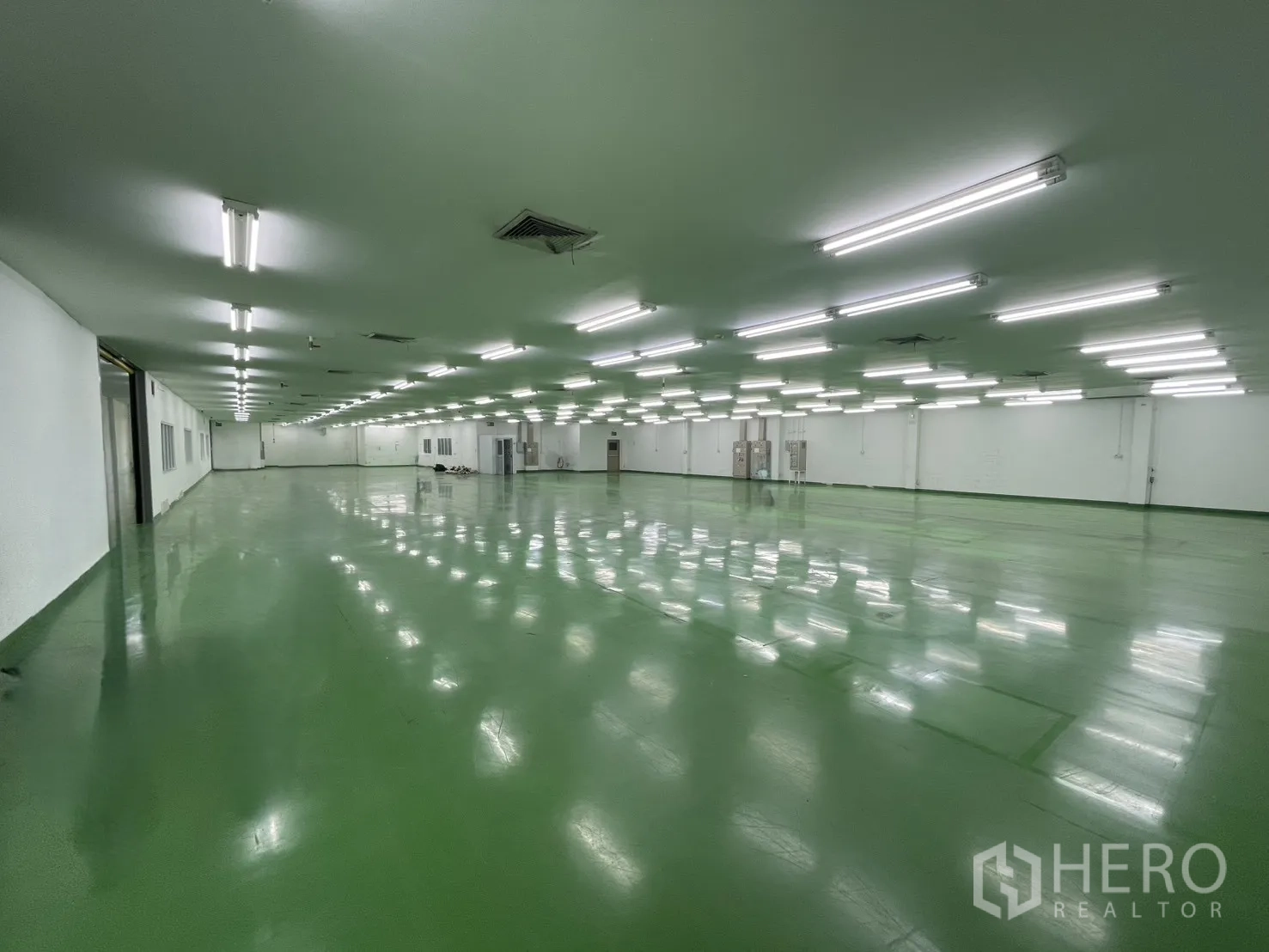 Factory for rent in Mueang Samut Prakan, Samut Prakan - Wide production hall with reflective green floor, ceiling ventilation panels and rows of strip lights.