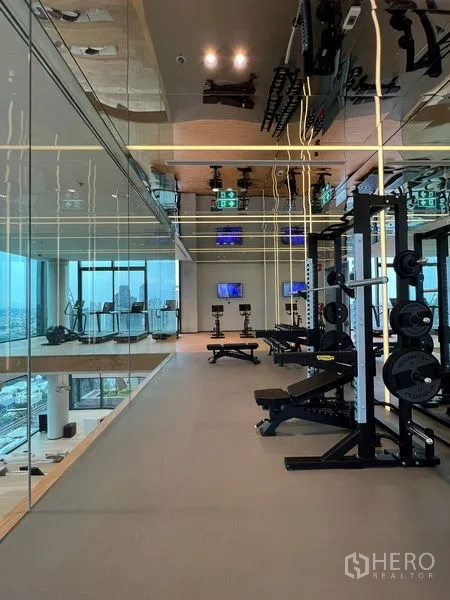 Condominium for rent in Bang Rak, Bangkok - Glass-walled fitness center with weights and cardio equipment, city view.