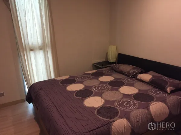 Condominium for rent in Watthana, Bangkok - Cozy bedroom with king bed, patterned duvet, bedside lamp, and warm wood flooring.