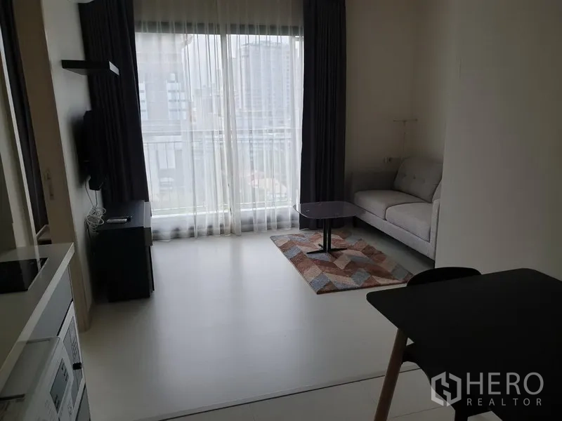 คอนโด ให้เช่าในKhlong Toei, Bangkok - ห้องนั่งเล่นสว่างด้วยหน้าต่างเต็มบาน ผ้าม่านสองชั้น โซฟาสีเทา และโต๊ะกลาง พร้อมวิวเมือง ในคอนโดใกล้ BTS ทองหล่อ เขตคลองเตย