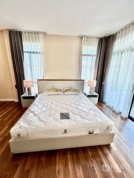 Detached House for rent or sale in Prawet, Bangkok - Master bedroom with king bed, bedside tables, floor-to-ceiling corner windows and balcony access.