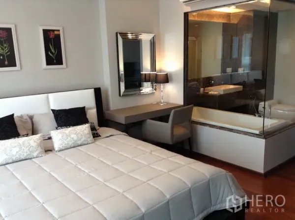 Condominium for rent in Watthana, Bangkok - Master bedroom with upholstered headboard, work desk and glass-walled bathroom featuring a bathtub.