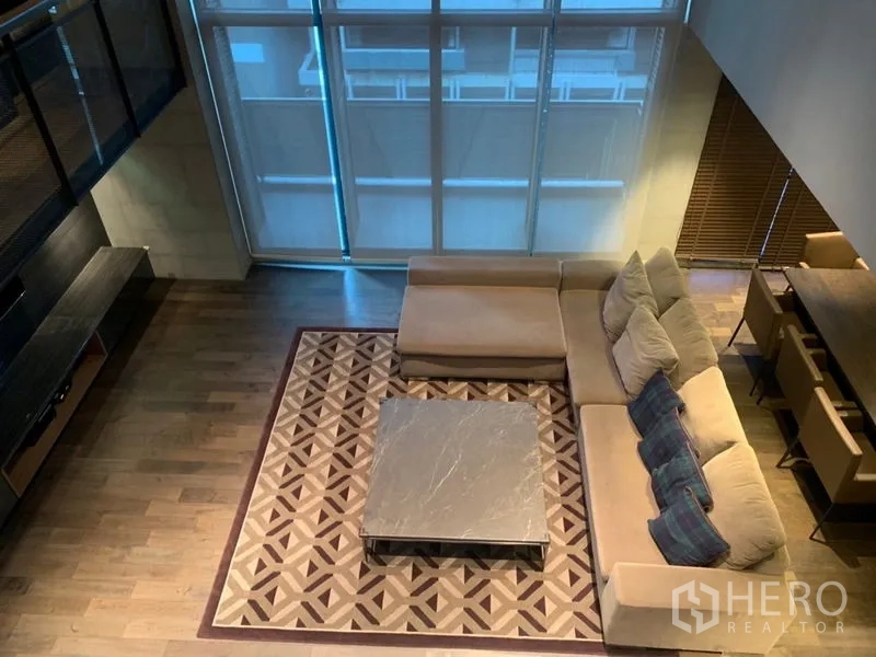 คอนโด ให้เช่าในWatthana, Bangkok - มุมมองจากด้านบน โซฟา L‑shape บนพรมลายเรขาคณิต ข้างหน้าต่างสูง